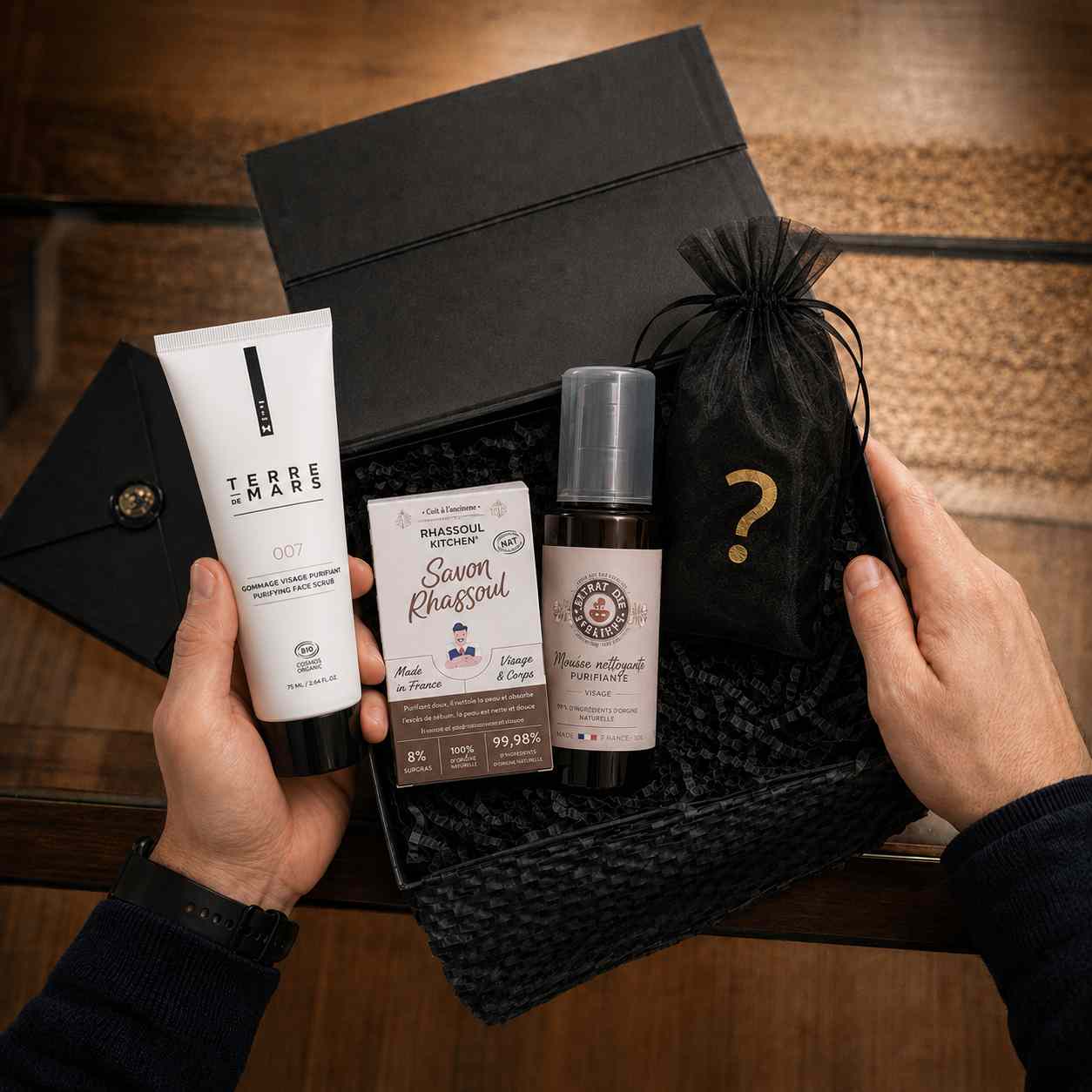Coffret cadeau pour homme tenu dans les mains, contenant un gommage Terre de Mars, un savon au rhassoul et un produit mystère.